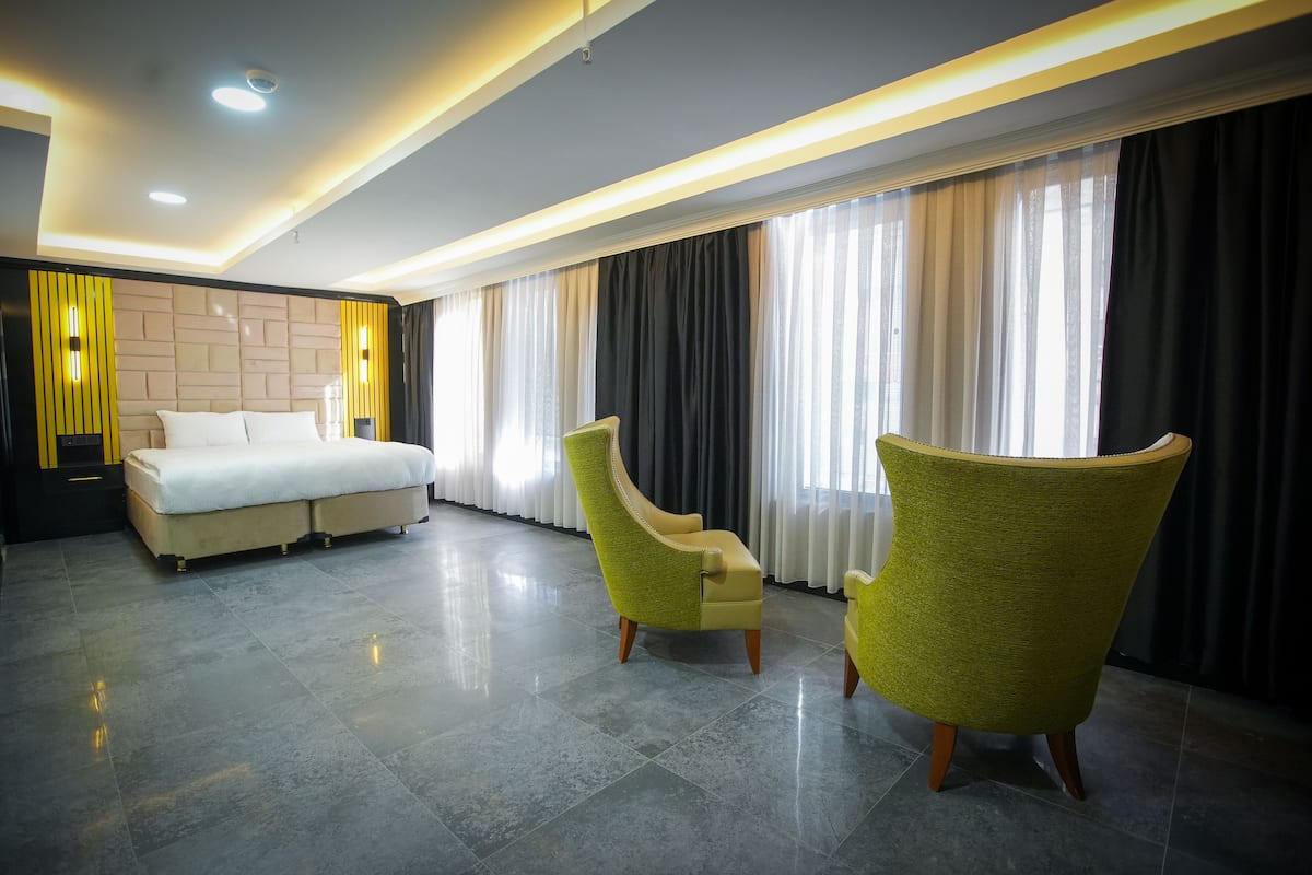 A modern hotel room with a bed, two armchairs, and a large window with curtains.