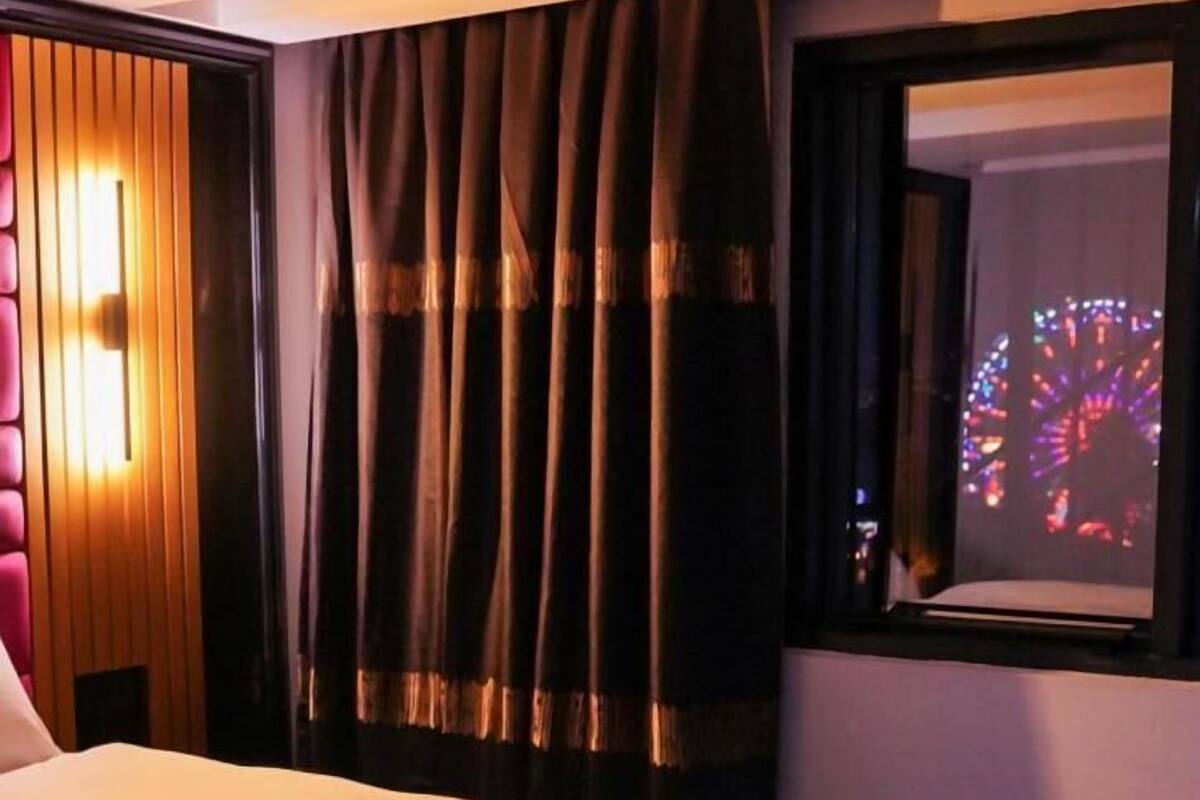 A hotel room with a large bed, a wooden panel wall, a window with curtains, and a view of a Ferris wheel.