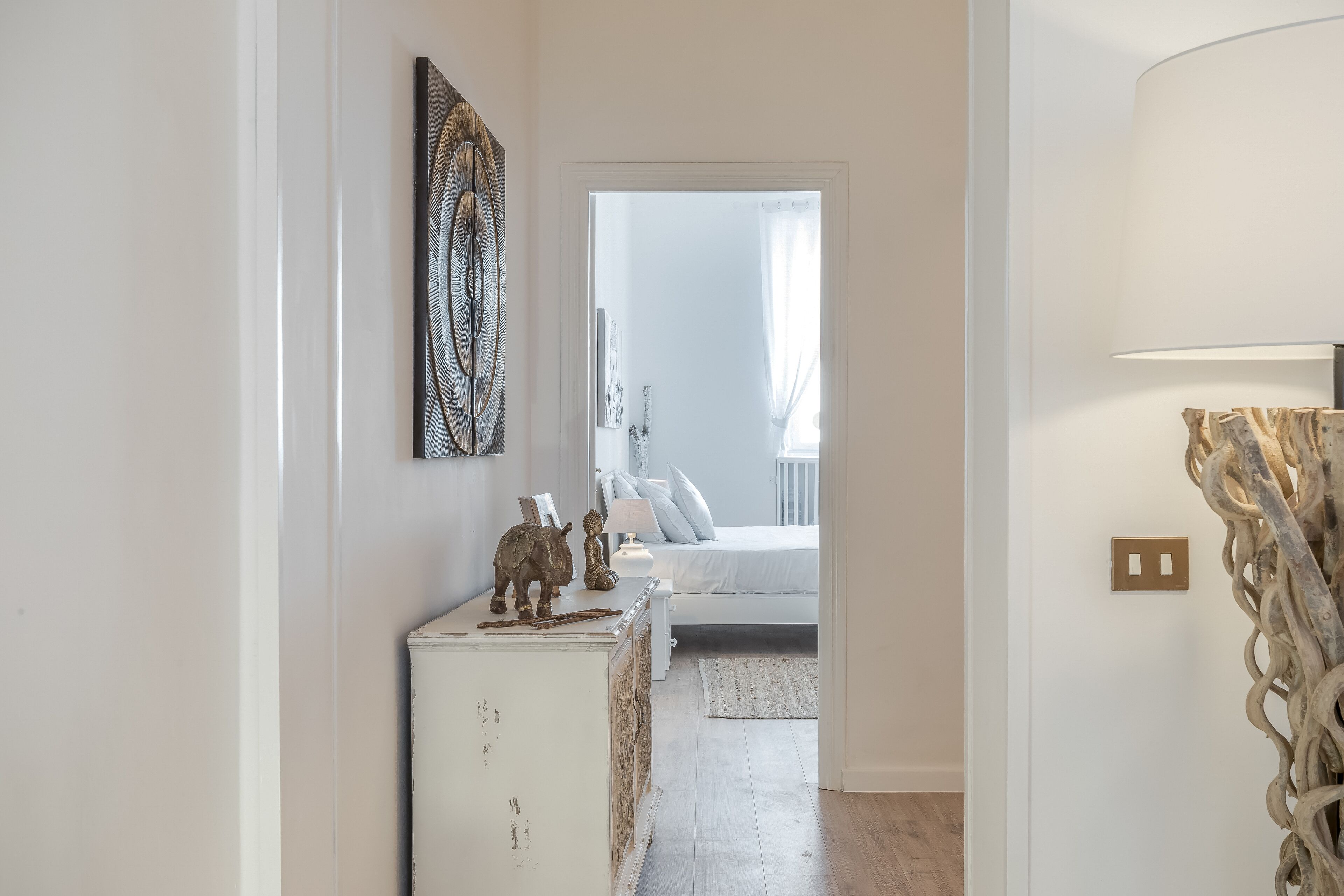 Un pasillo que conduce a un dormitorio con una cama, un tocador y una lámpara.