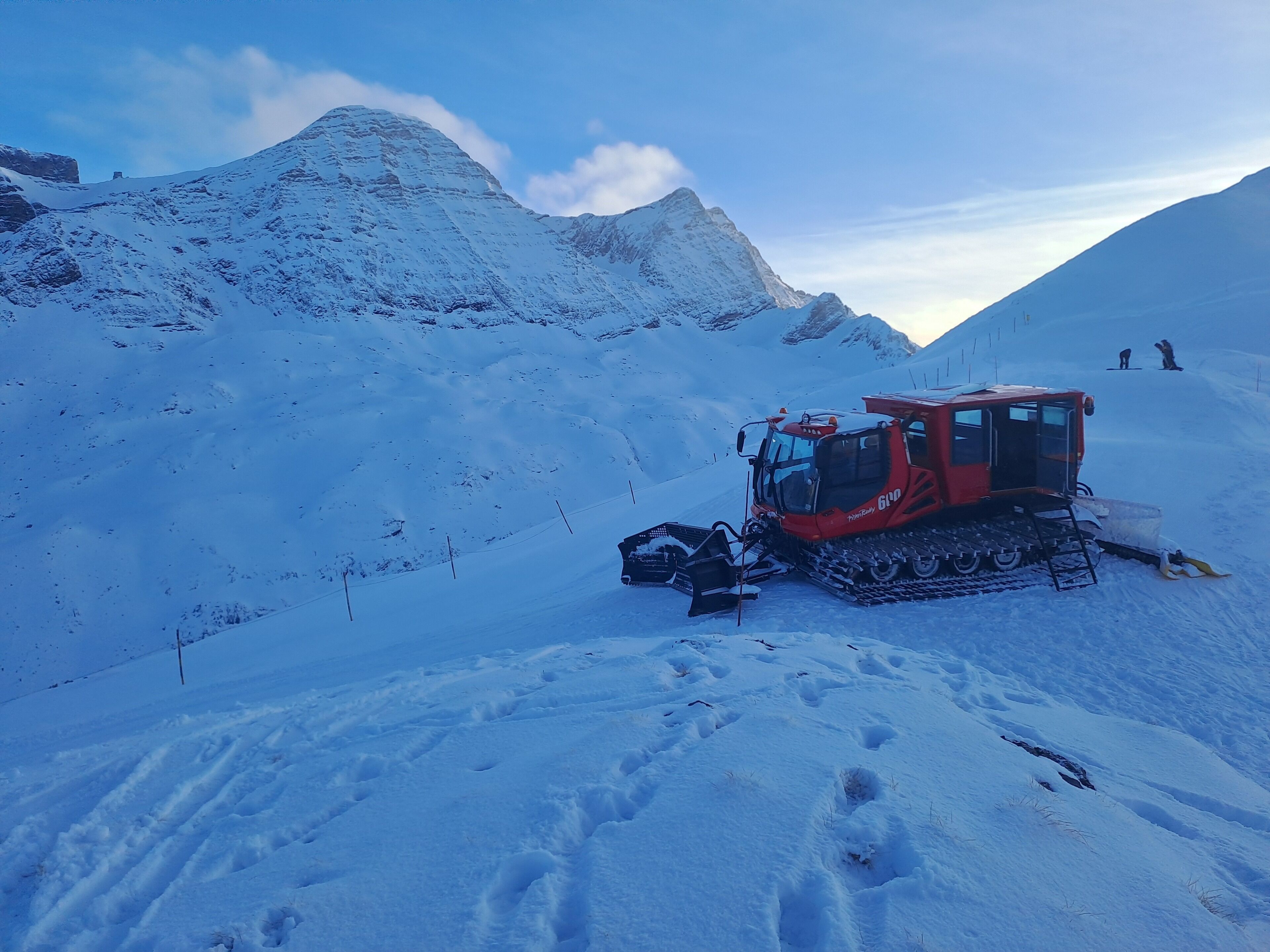 A red tracked vehicle on a snowy mountain slope with footprints leading up to it.