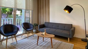A modern living room with a grey sofa, two dark armchairs, a small wooden coffee table, and a floor lamp. - w* | Bright 2BR Duplex with Balcony in Barranco (Barranco)