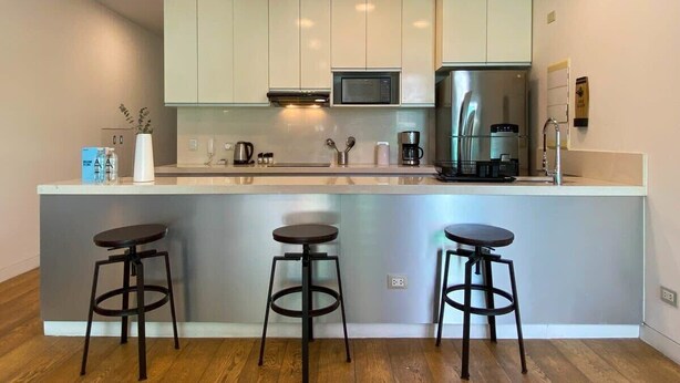 A modern kitchen with white cabinets, a stainless steel refrigerator, a microwave, and a coffee machine. There are three stools at the counter. - w* | Bright 2BR Duplex with Balcony in Barranco (Barranco)