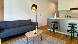 A modern living room with a sofa, a coffee table, and a lamp. There is a kitchen area with a counter and stools. - w* | Bright 2BR Duplex with Balcony in Barranco (Barranco)