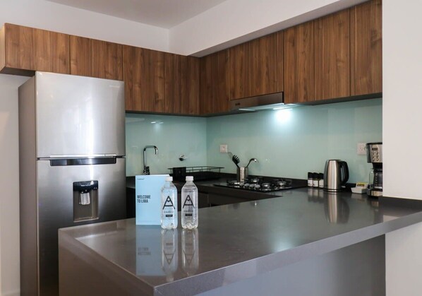 A modern kitchen with wooden cabinets, a stainless steel refrigerator, a water dispenser, a coffee maker, and two bottles of water on the counter.
