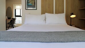 A hotel room with a large bed, a desk with a chair, a framed picture on the wall, and a bedside lamp.