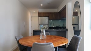 A modern dining area with a round wooden table, grey upholstered chairs, and a vase with flowers.