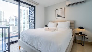 A modern hotel room with a large bed, a city view through a sliding door, a small table with a lamp, and an air conditioning unit on the wall. - w* | Refined 1BR in San Francisco (Panamá)