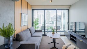 A modern living room with a grey sofa, a small round table, a TV, and a large window with a city view. - w* | Refined 1BR in San Francisco (Panamá)