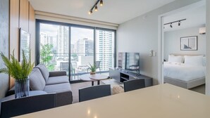 A modern hotel room with a large window, a sofa, a dining table, a TV, and a bed. - w* | Refined 1BR in San Francisco (Panamá)