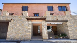 A two-story building with a stone facade, a sign for 'Taller de Cerámica', and a small entrance with potted plants. - APARTAMENTOS CREATIVOS VILLARUBEI (Villarroya de los Pinares)