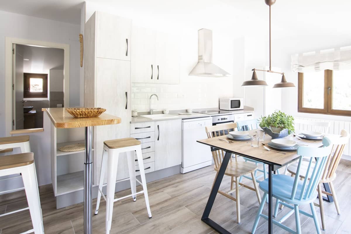 A modern kitchen with white cabinets, a central island, and a dining area with blue chairs.