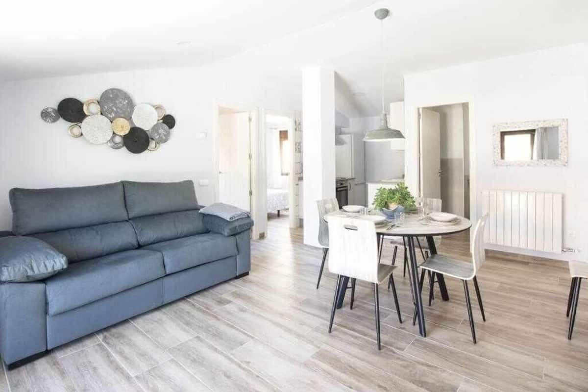 A modern living room with a grey sofa, a dining table with chairs, and a wall-mounted abstract art piece.