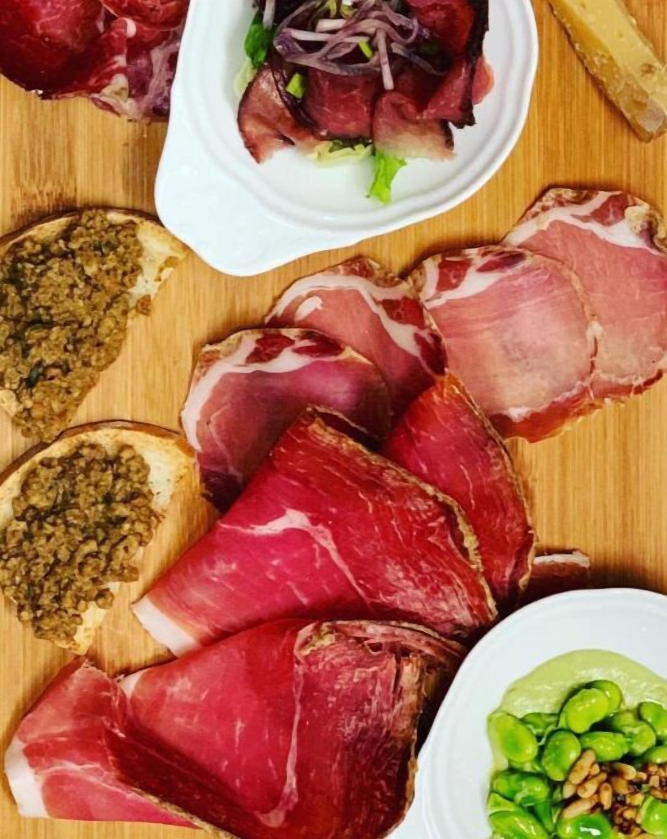 A variety of cured meats, including prosciutto and salami, arranged on a wooden board.