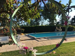 Ein Schwimmbecken mit einem kreisförmigen Gartenbrunnen, umgeben von einer Hecke und einem gepflegten Rasen.