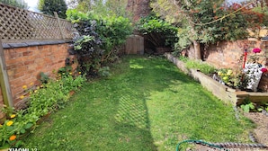 A well-maintained garden with a brick wall, a wooden fence, and various plants and flowers. - St Lucia guest house (Leicester)