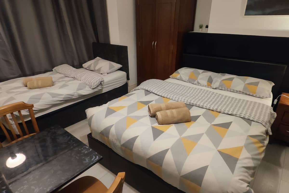 A hotel room with two beds, a dining table, and a wooden wardrobe.