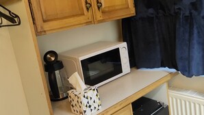 A compact kitchen with wooden cabinets, a microwave, a coffee maker, and a small refrigerator. - St Lucia guest house (Leicester)