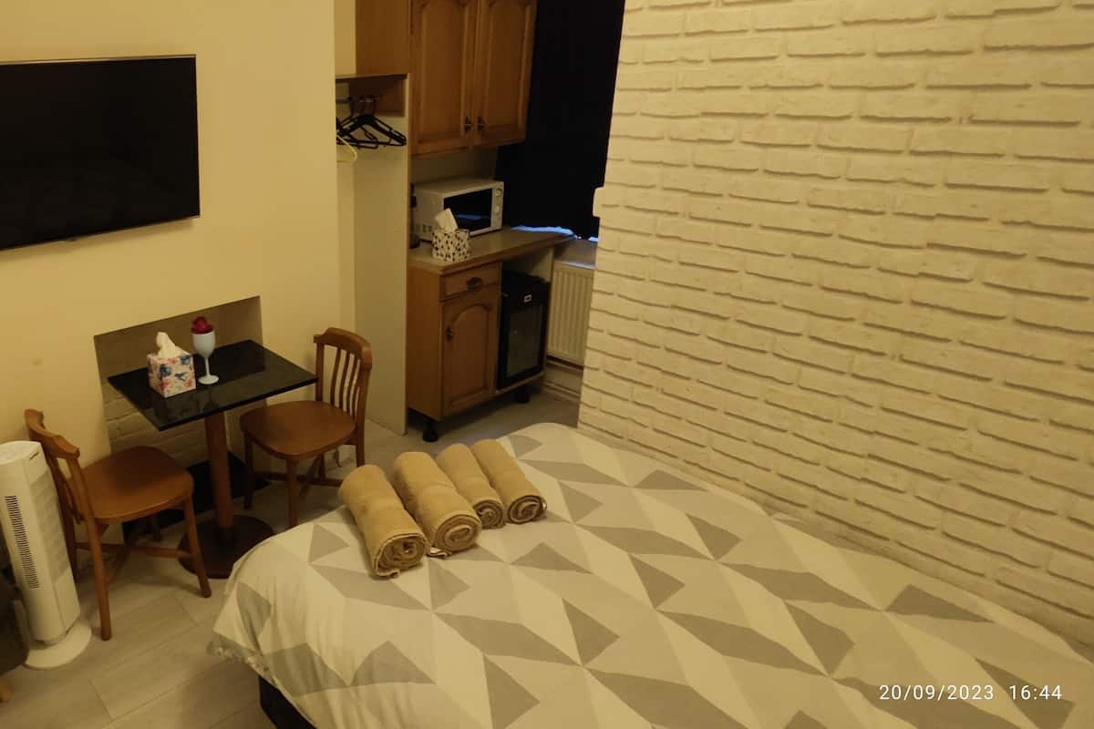 A compact hotel room with a sofa, a small table with chairs, a TV mounted on the wall, a microwave, and a brick-patterned wall.