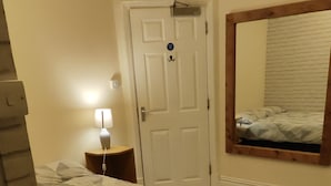 A bedroom with a bed, a nightstand, a lamp, a door, and a mirror. - St Lucia guest house (Leicester)