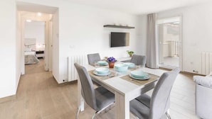 Un espace repas moderne avec une table en bois dressée pour quatre personnes, des chaises à revêtement gris et une plante en pot posée sur la table.