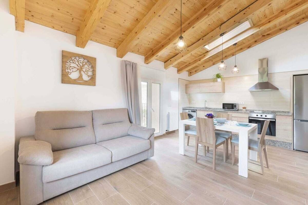 A modern living room with a sofa, a dining table with chairs, and a kitchen area with a stove and refrigerator.