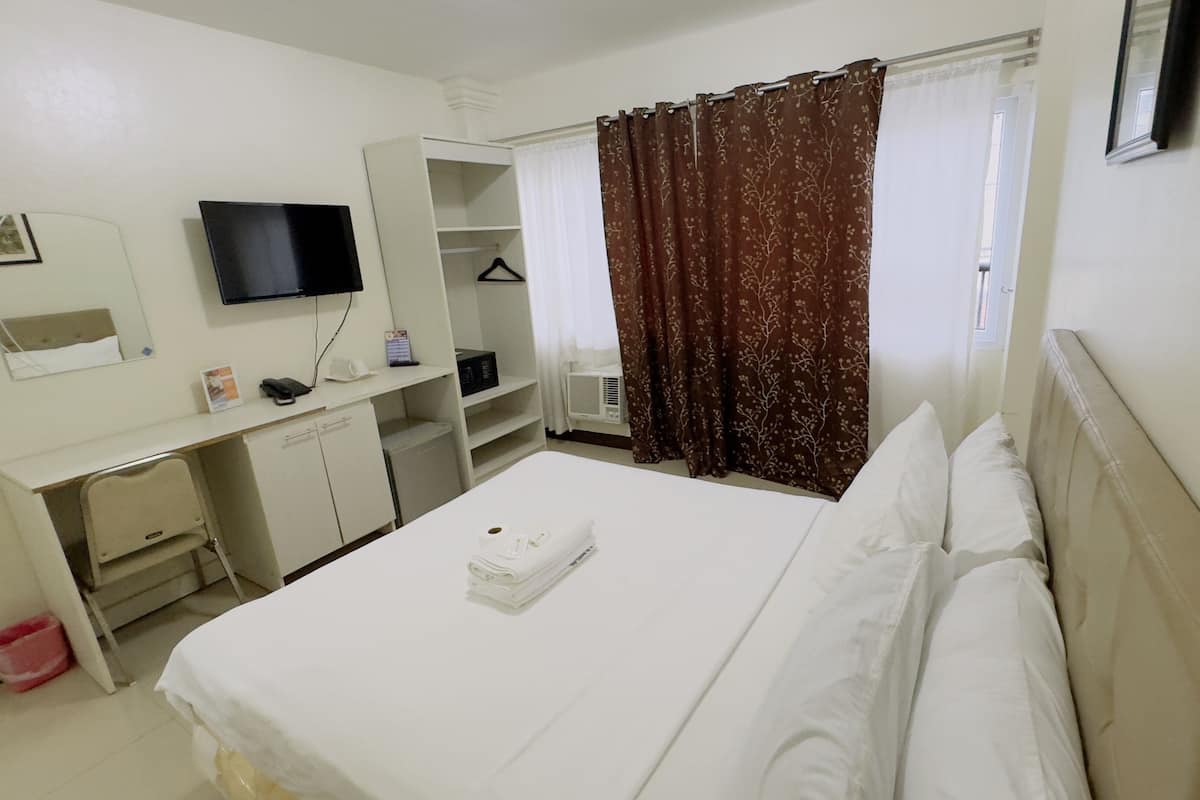Ein Hotelzimmer mit Bett, Schreibtisch, Stuhl, Fernseher, Kleiderschrank und einem Fenster mit Vorhängen.