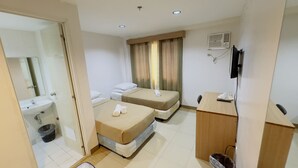 A hotel room with two single beds, a wooden desk, a TV, a bathroom with a sink and mirror, and a trash bin. - La Anclar Hotel (Davao)
