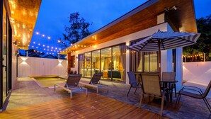A modern outdoor patio with a wooden deck, lounge chairs, a table with chairs, and string lights. - Fishermen Pool Villa Samui (Chang Wat Surat Thani)