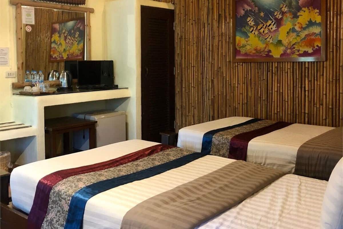 A hotel room with two beds, a desk with a computer, a television, and a wall-mounted air conditioner.