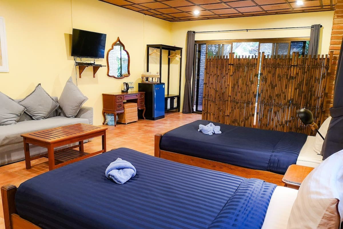 A hotel room with two beds, a sofa, a TV, a desk, and a window with a view.