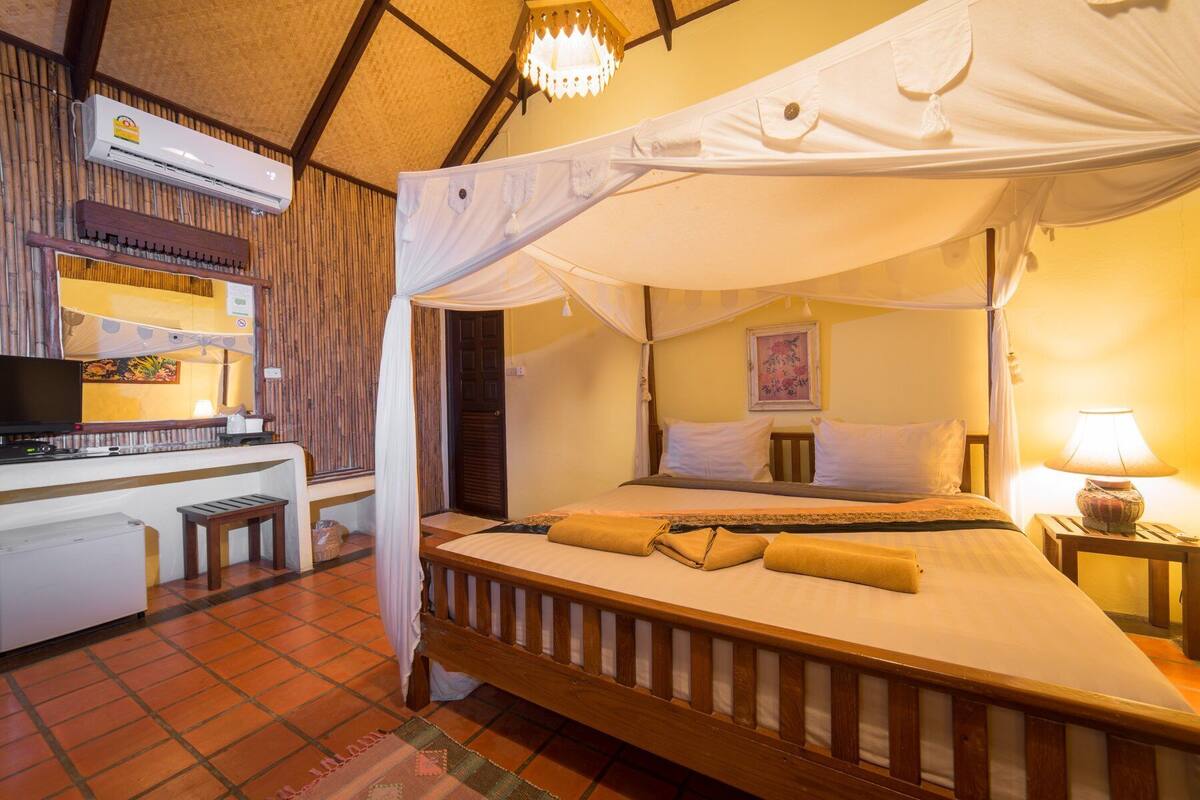 A room with a bed under a canopy, a desk with a computer, and a television.