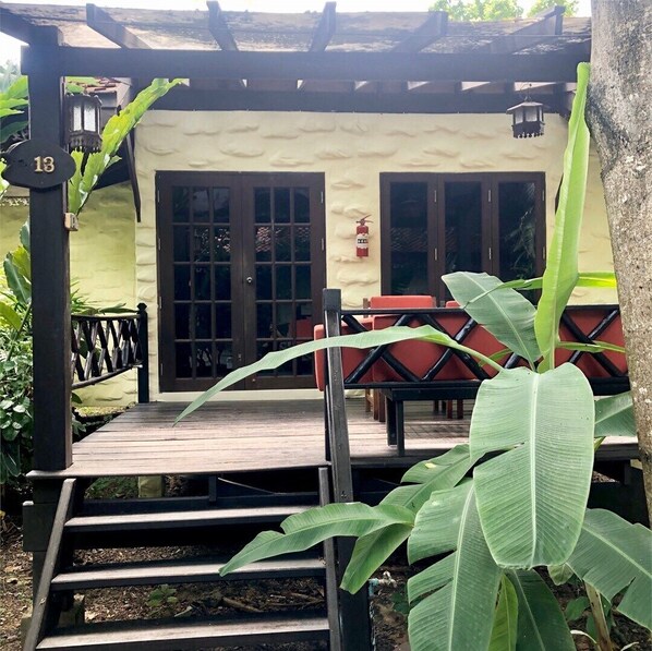 Un área de estar al aire libre cubierta con piso de madera, una puerta con paneles de vidrio y un extintor montado en la pared.