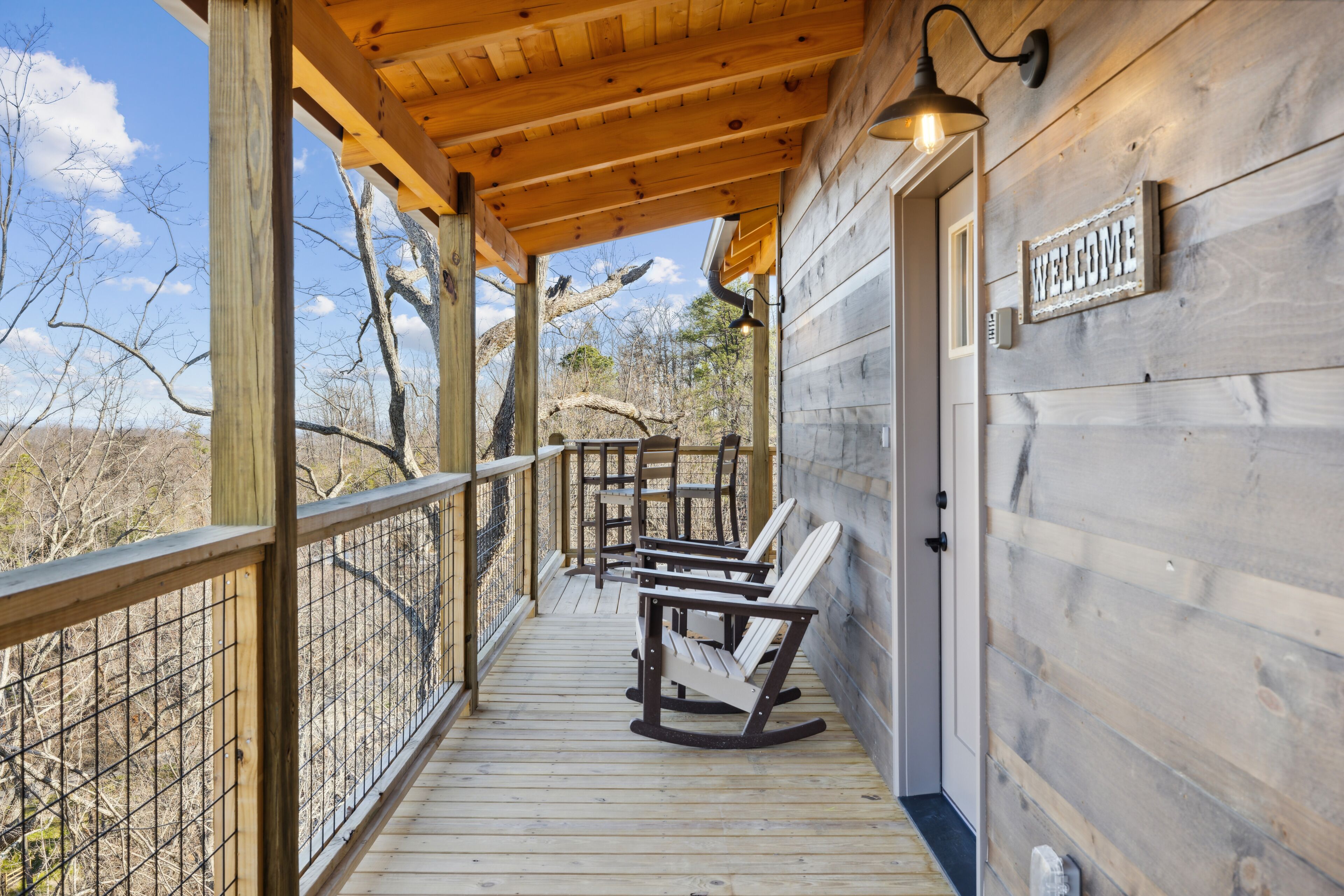 A wooden deck with rocking chairs and a 'WELCOME' sign, overlooking a natural landscape.