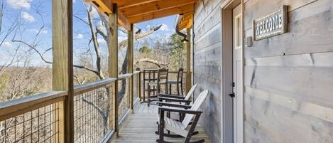 A wooden deck with rocking chairs and a 'WELCOME' sign, overlooking a natural landscape.
