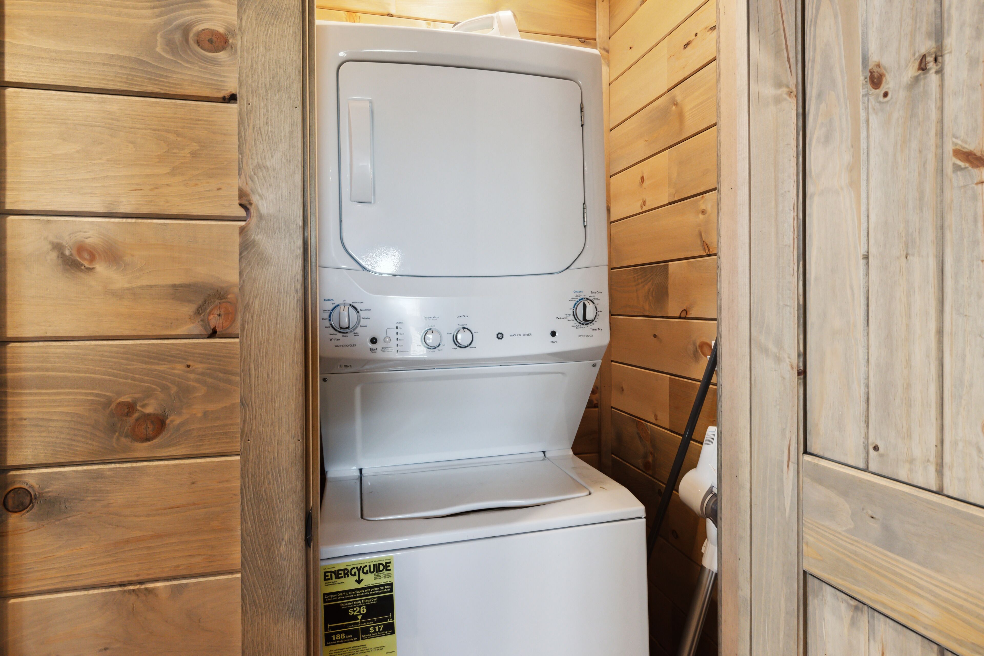 Un appareil compact, blanc, combinant lave-linge et sèche-linge à chargement frontal, installé dans une pièce aménagée dans le style d’un chalet en bois.