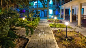 Ein Gartenweg bei Nacht, der zu einem Gebäude mit Balkon und Sitzgelegenheit im Freien führt.