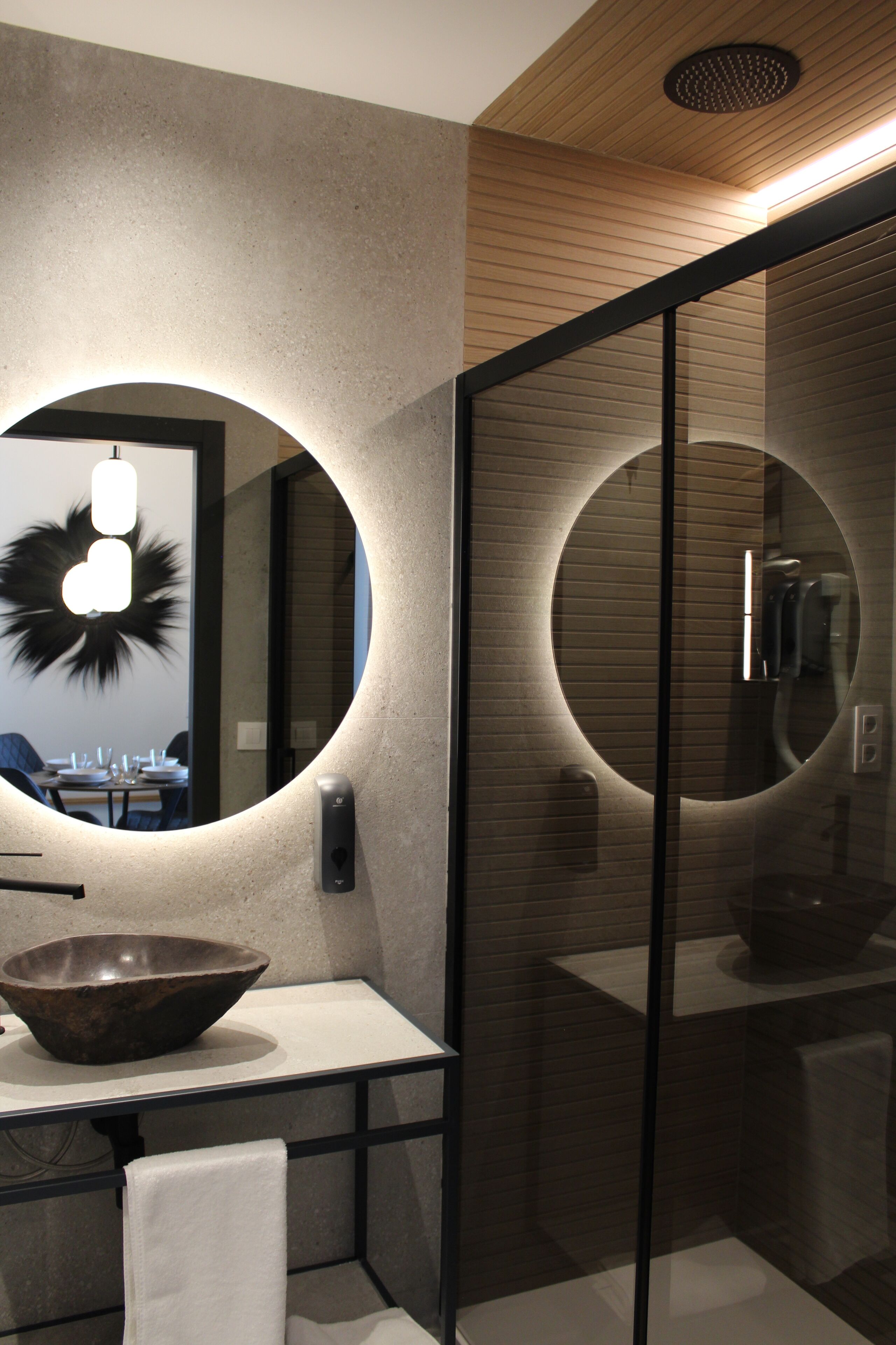 A modern bathroom with a round mirror, a bowl sink, and a glass shower enclosure.