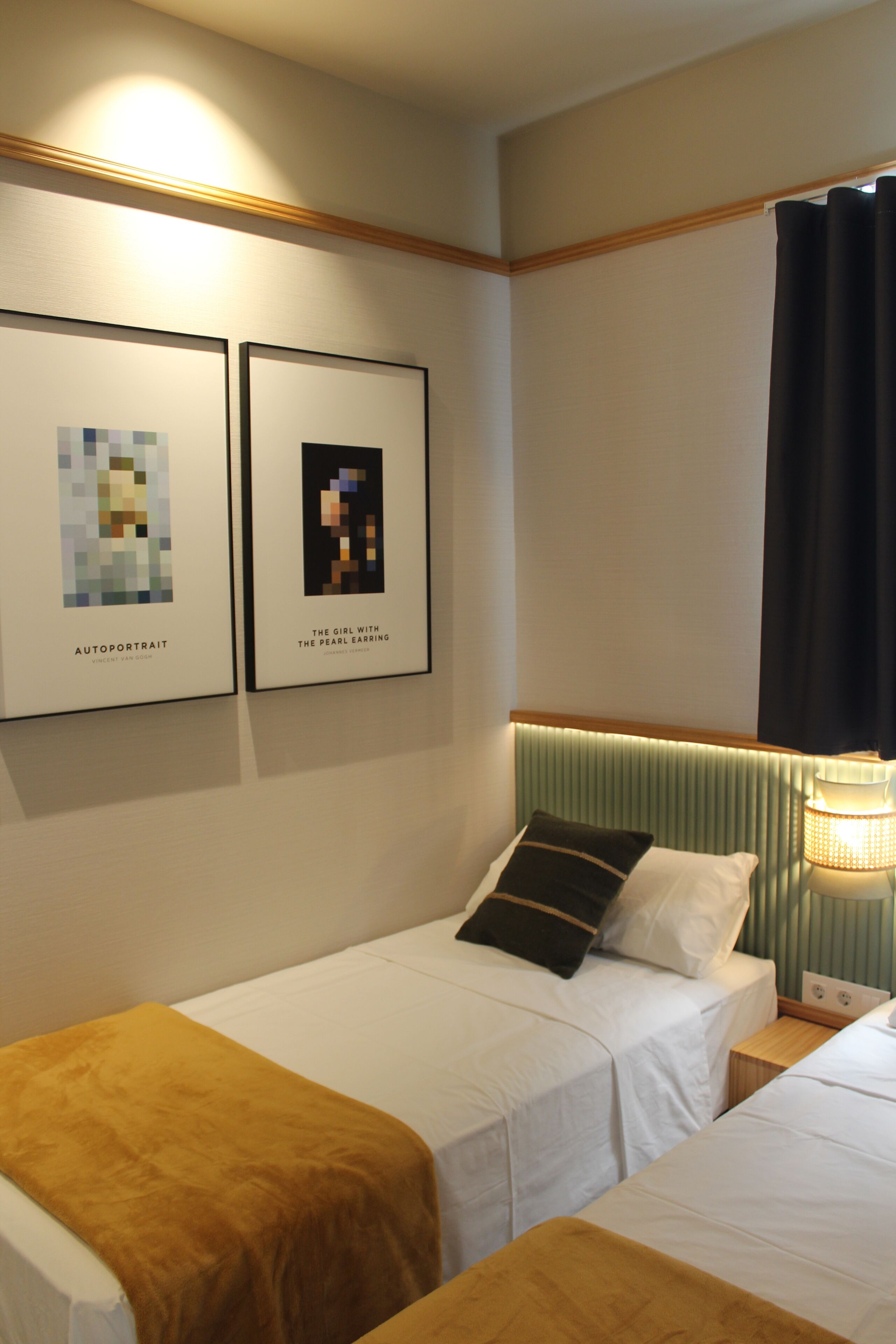 Una habitación de hotel con dos camas individuales, una mesita de noche con lámpara y dos cuadros enmarcados en la pared.