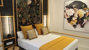 A neatly made bed with a white mattress and a mustard-colored blanket, flanked by two pillows, in a room with a dark wood panel design and a large floral artwork on the wall. - Promotur Suites - Ayora (Valencia)