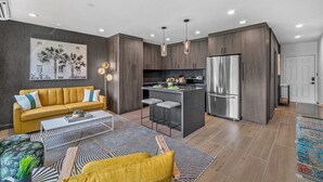 A modern kitchen with a stainless steel refrigerator, a dining area with a yellow sofa and patterned rug, and a kitchen island with bar stools. - 261 #5 Managed By Brampton Park (Deerfield Beach)