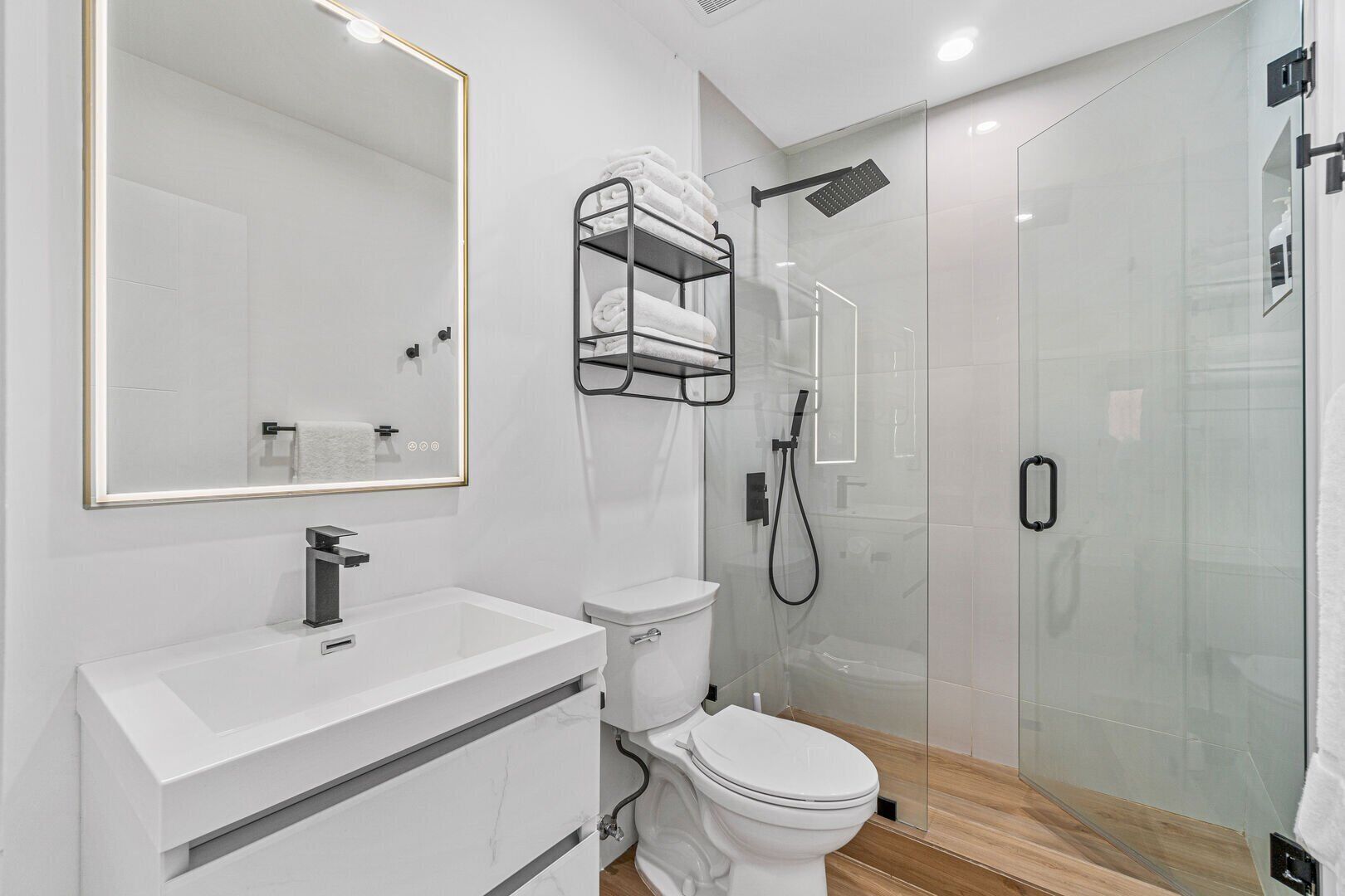 Une salle de bain moderne avec un meuble-lavabo blanc, des toilettes, une douche en verre et un porte-serviettes.