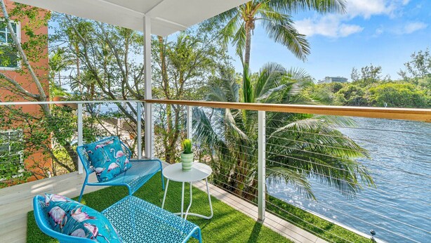 Un balcon donnant sur une rivière, entouré de palmiers et d’un immeuble.