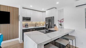 Une cuisine moderne dotée d’un plan de travail en marbre, d’appareils électroménagers en acier inoxydable et d’un mur d’accent en bois.