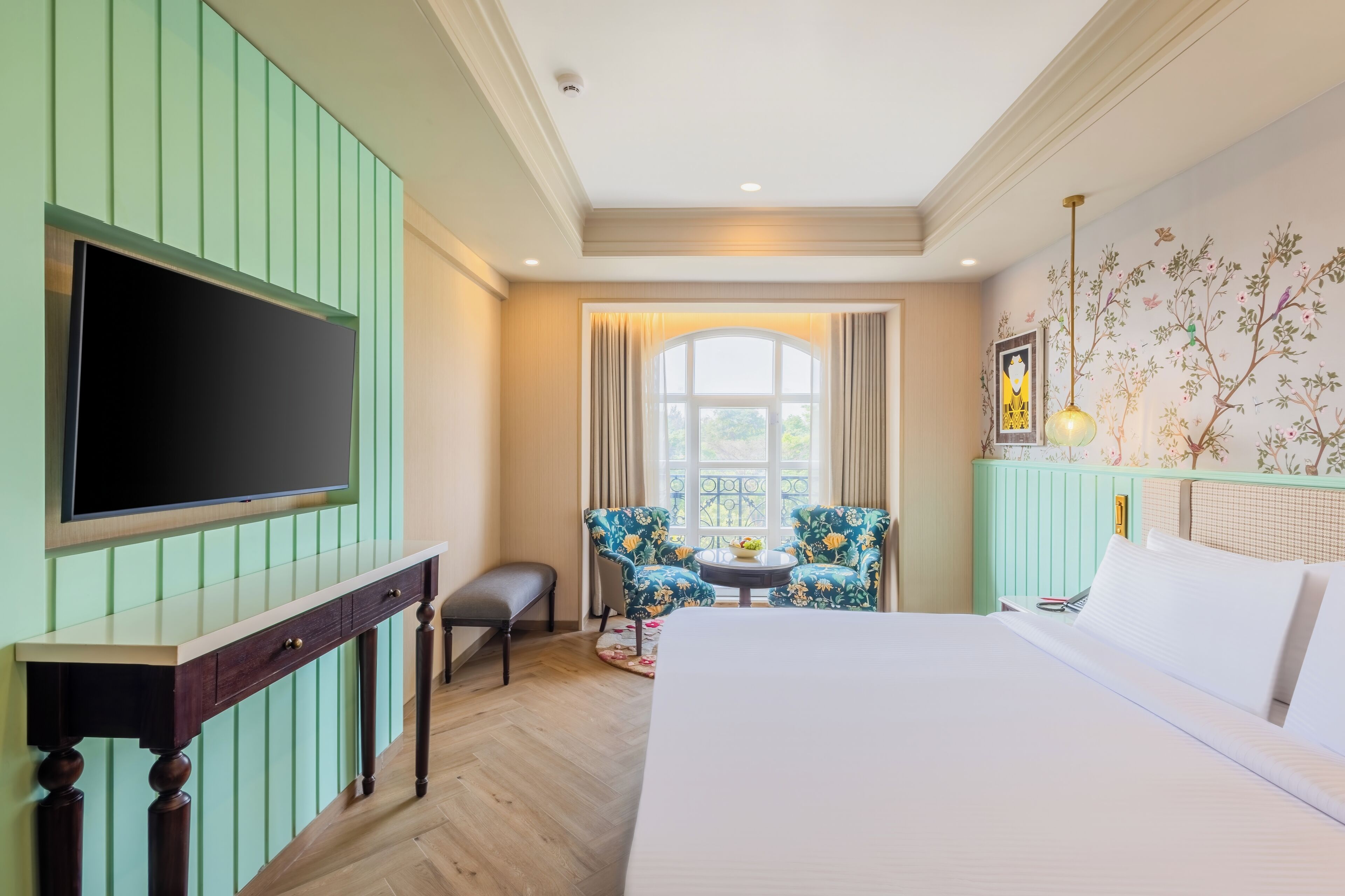 Habitación de hotel con cama, televisión montada en la pared, una mesita con sillas y ventana con cortinas.
