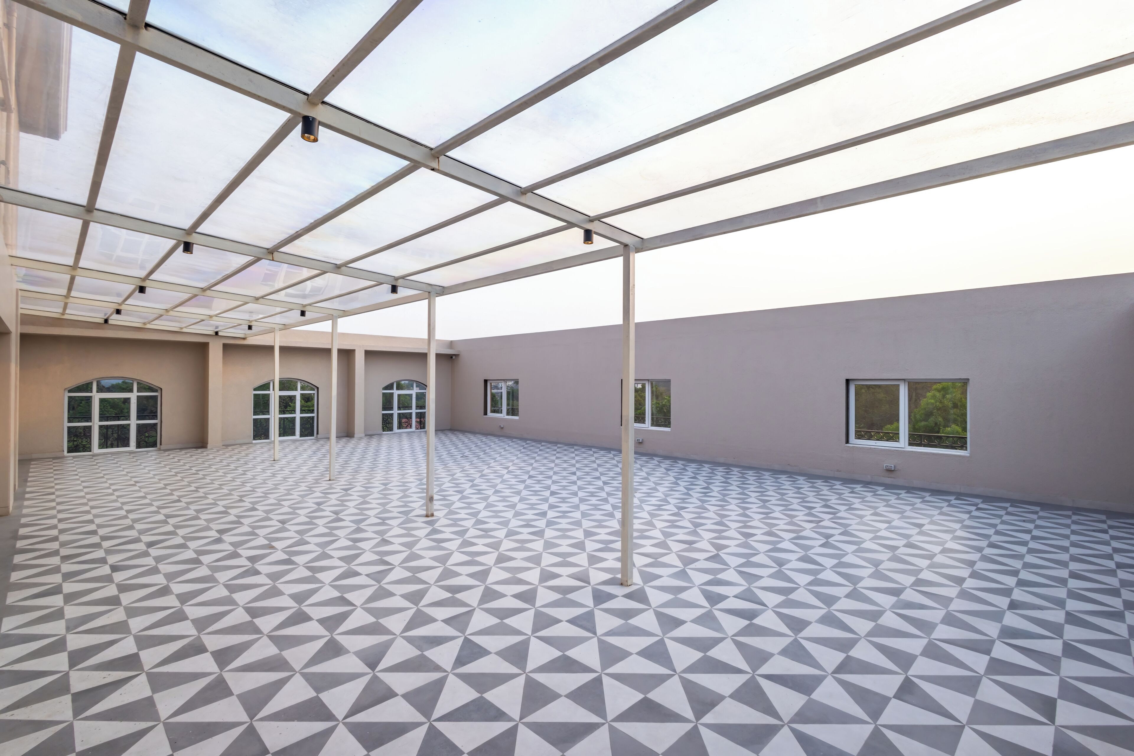 A spacious indoor area with a geometric patterned floor, large windows, and a metal ceiling structure.