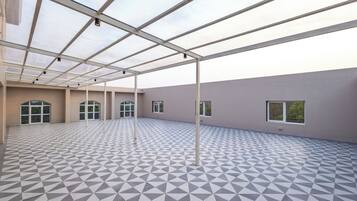 A spacious indoor area with a geometric patterned floor, large windows, and a metal ceiling structure.