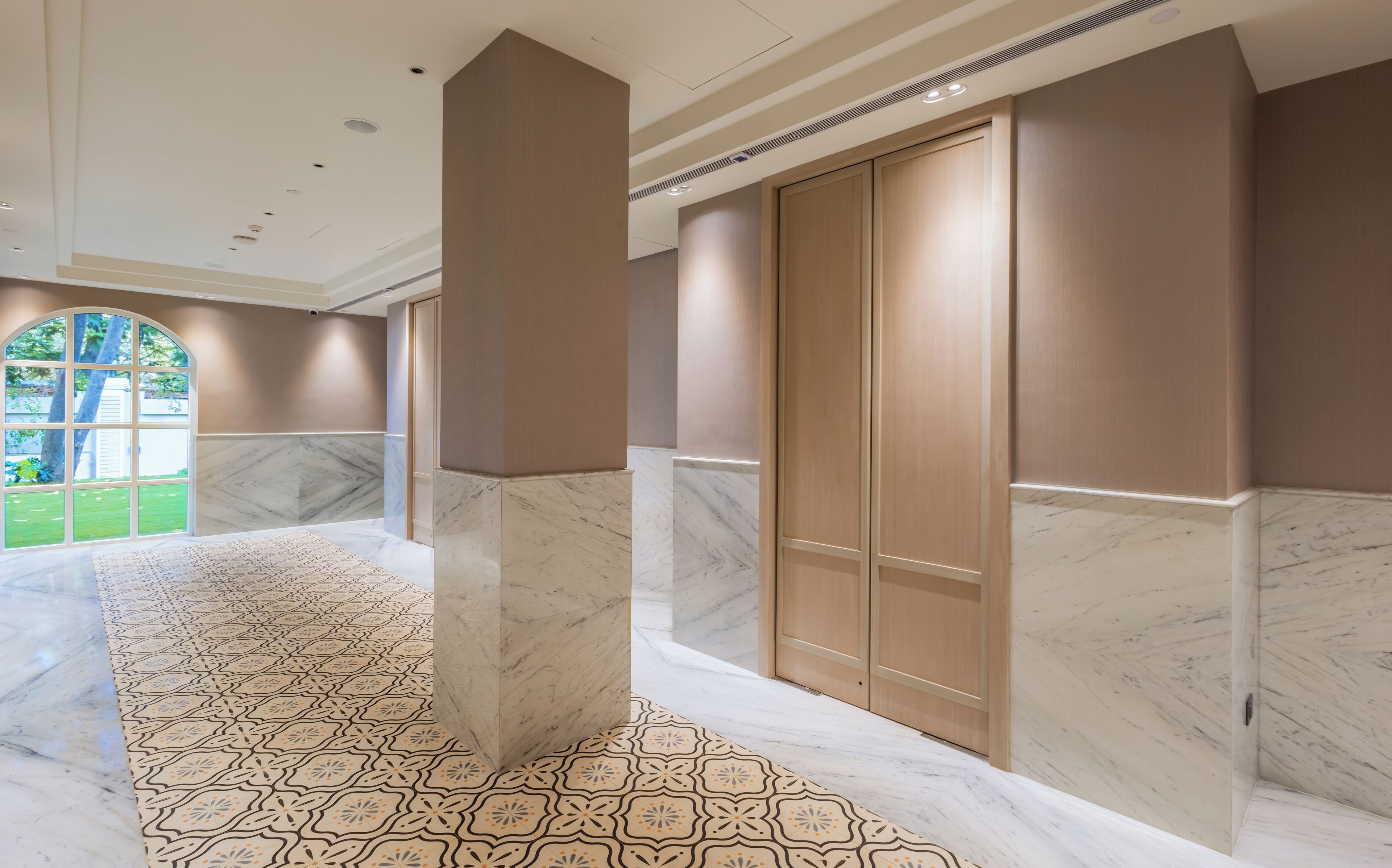 A spacious hallway with marble flooring and a large arched window.