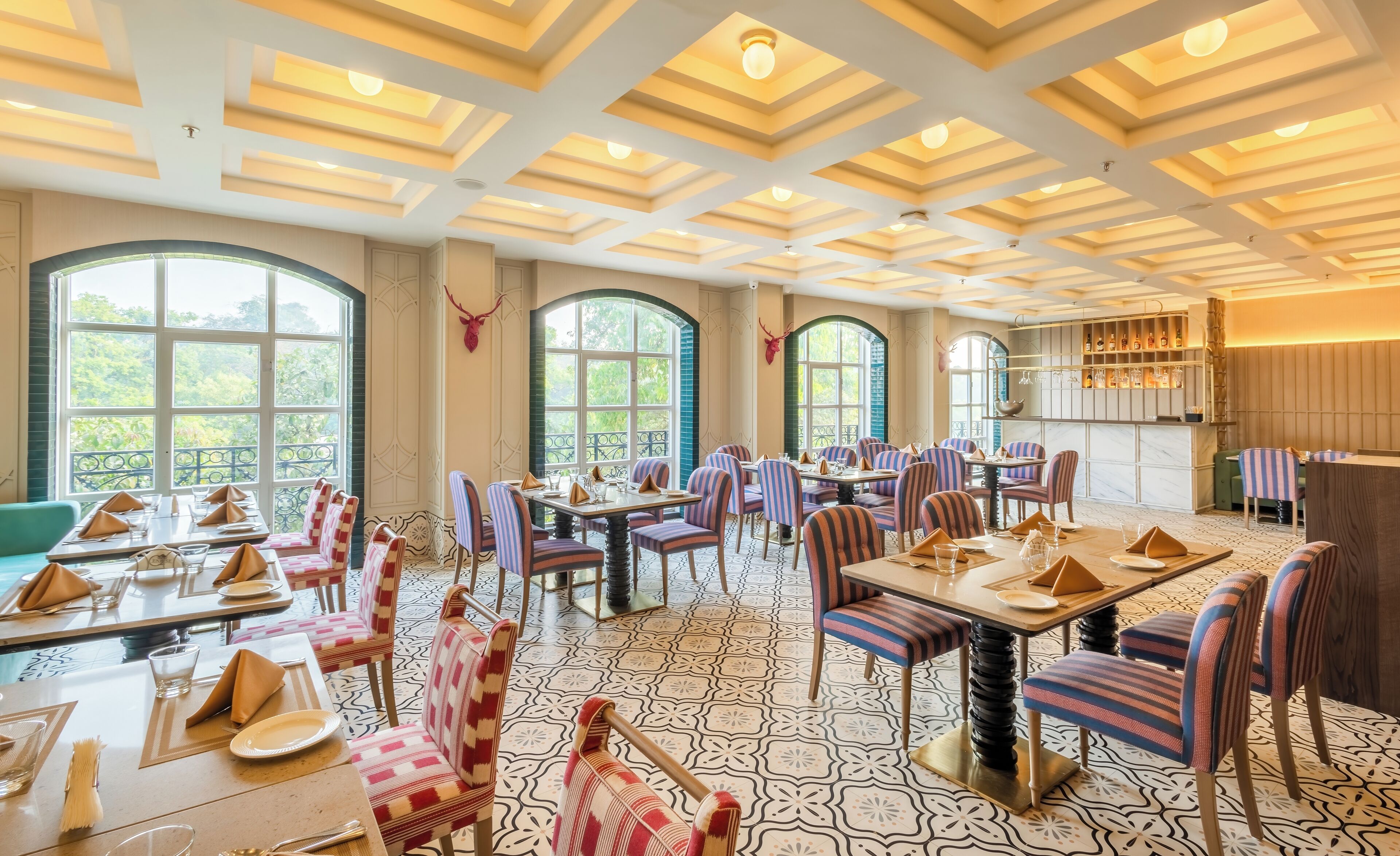A spacious dining area with high ceilings, large windows, and striped chairs. Tables are set with plates and napkins.