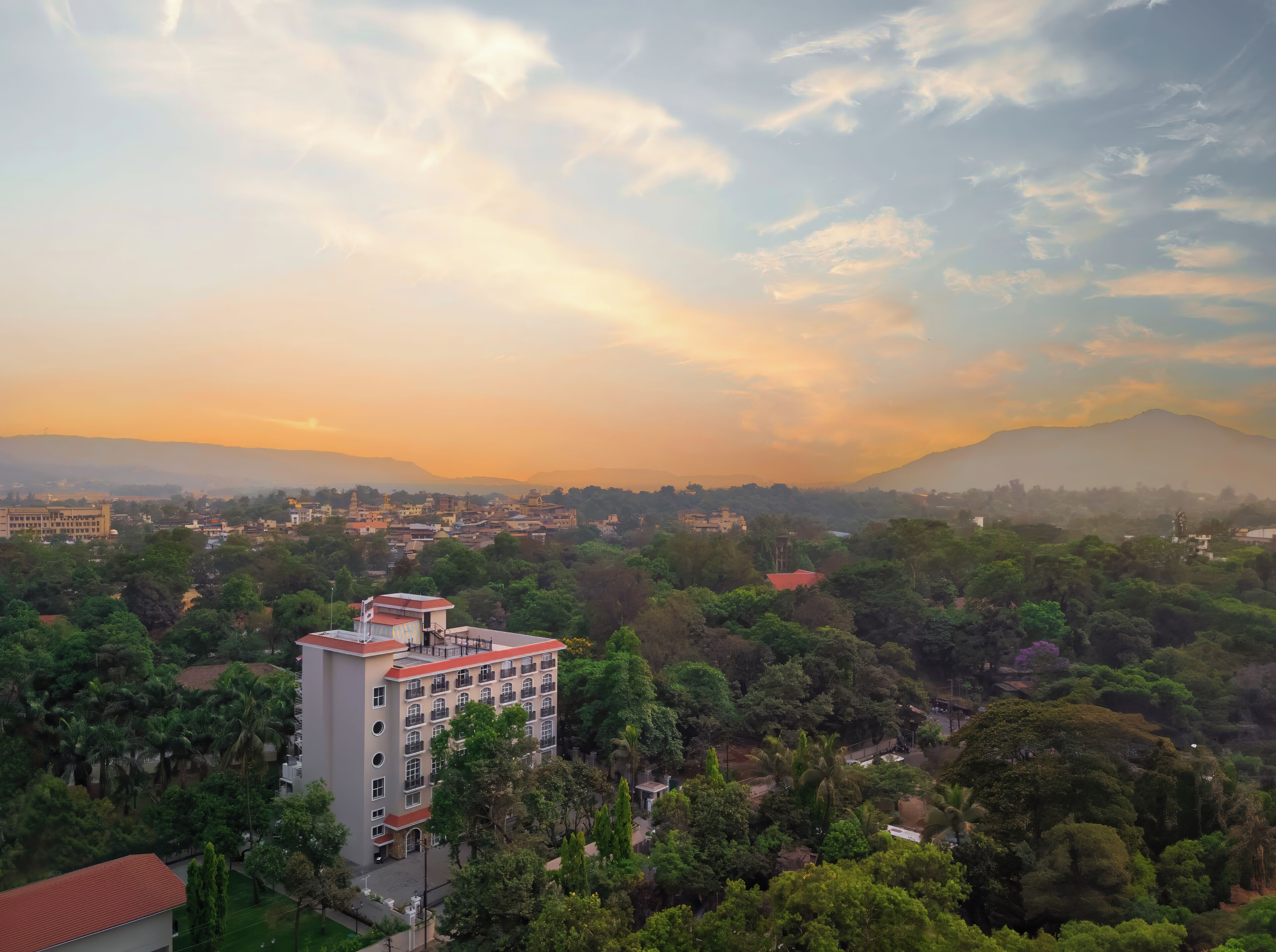 A hotel with multiple floors, surrounded by lush greenery and a mountainous backdrop.