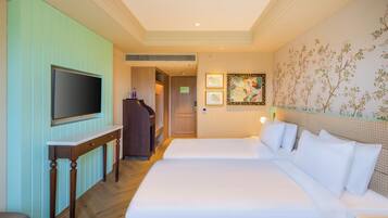 A hotel room with a large bed, a TV on a wooden stand, a desk, and a wall with floral wallpaper.